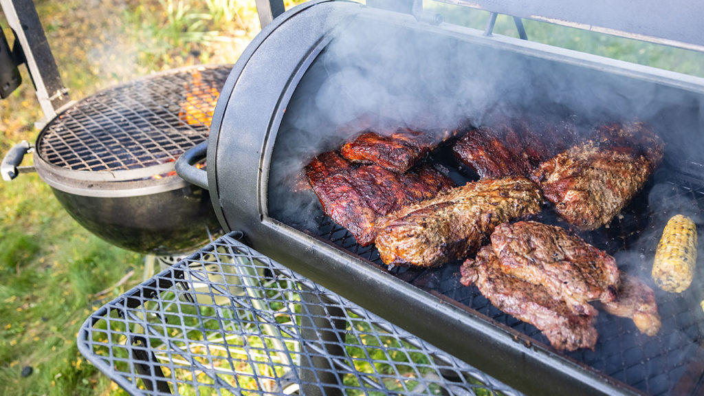 A smoker open and full of beef and corn.